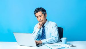 パソコンに向かい、ビジネスローンの即日融資や審査について検討する法人経営者または個人事業主、事業資金の調達方法を思案する様子