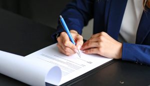 契約書に署名するビジネスウーマンの手元、ファクタリング契約における手数料や金利の相場を確認する場面