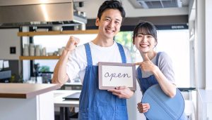 金融機関からの融資で事業資金を調達し、飲食店を開業した事業主が「open」の看板を掲げる様子