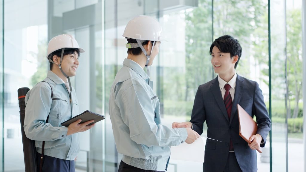 ヘルメットを被った作業員とスーツ姿の男性が現場で打ち合わせをしている様子。建設業などでビジネスローンの審査を即日で通過させ資金調達が必要な場面