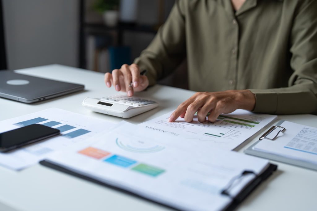 デスクに広げたグラフ付きの財務資料を確認しながら電卓を叩きファクタリングを利用した資金繰り計画を立てている手元