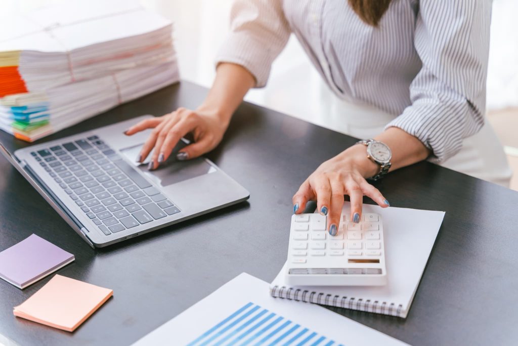 電卓を操作しながらパソコン画面を確認する女性。証書貸付とは元金均等返済などの返済方法があり長期的な返済計画の策定が必要な融資