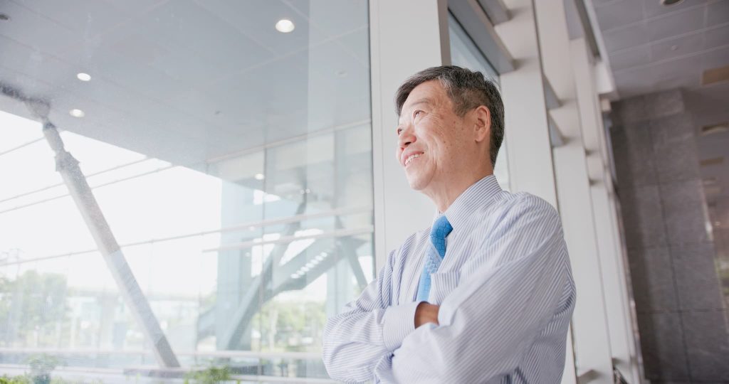 オフィスの窓際で腕を組み笑顔を見せる経営者風の男性。ビジネスローンの審査に通り即日で資金調達できたことで、事業の先行きに安心感を得た様子