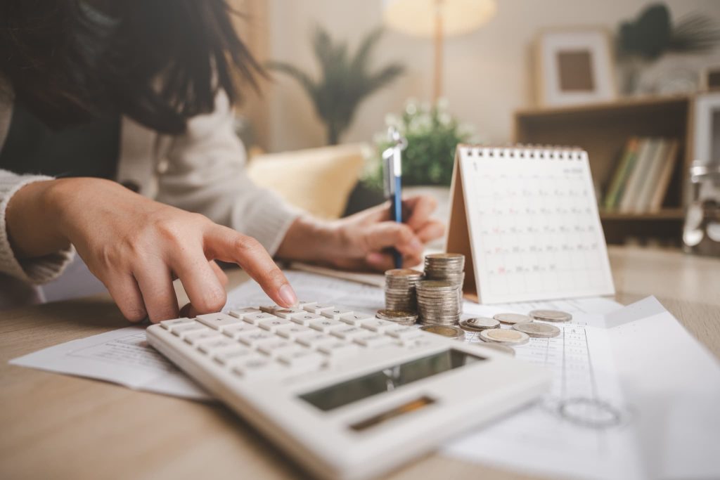 請求書カード払いサービスを利用して支払い期日を先延ばしにするためにカレンダーと硬貨を並べて資金繰りを確認している手元