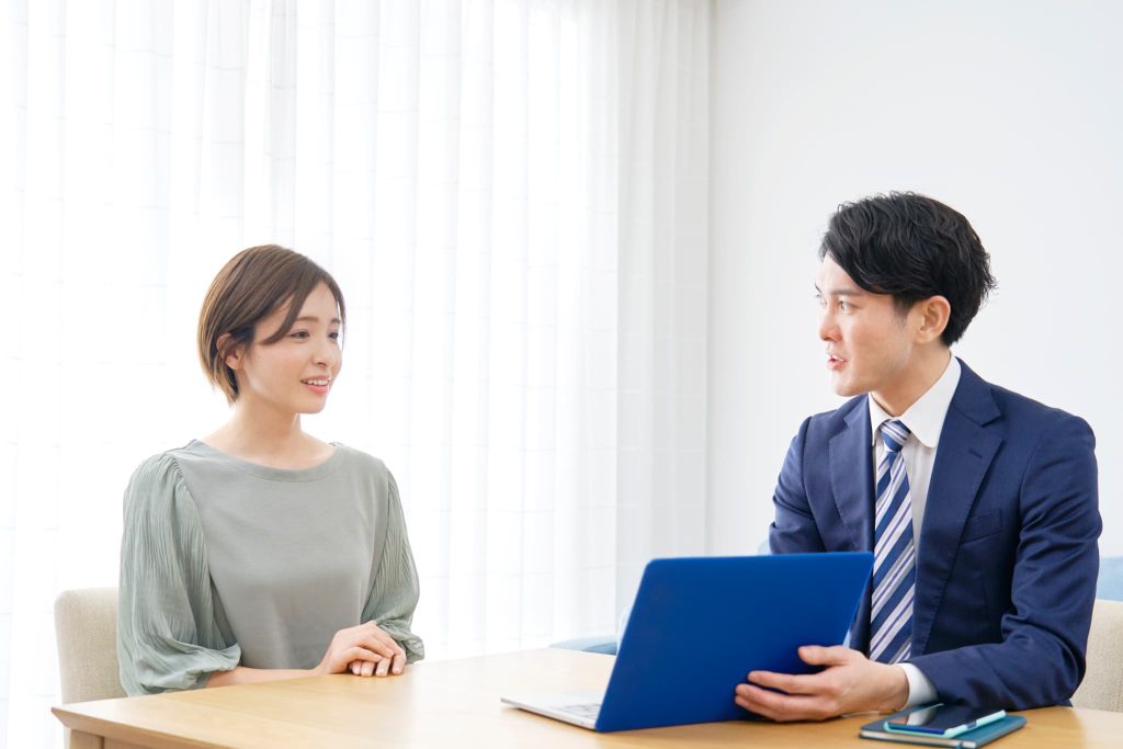 借り換え融資の手続きや独自のプランについてパソコン画面を見ながら担当者から説明を受けている女性