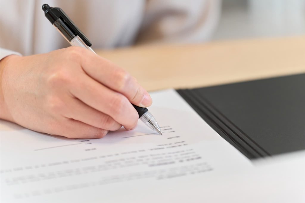 契約書にペンで署名を行っている手元。証書貸付とは金銭消費貸借契約書(借用書)を取り交わして融資を受ける契約形態であることを示すイメージ