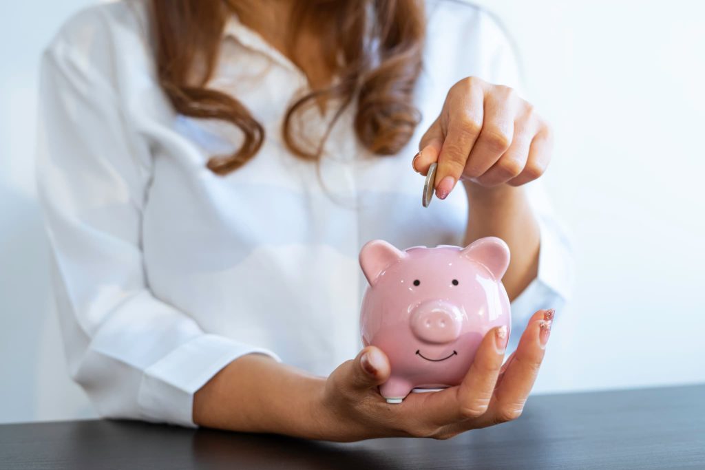 計画的な開業資金の準備として豚の貯金箱に硬貨を投入し貯蓄を行っている女性の手元