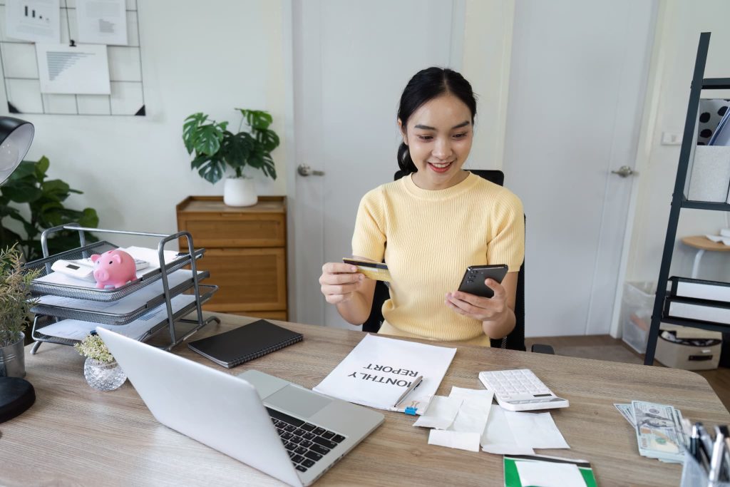 スマートフォンとクレジットカードを使って請求書の立替払いやオンライン決済を行っている女性