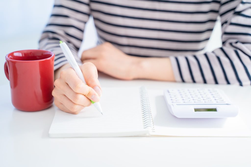 ノートと電卓を前にペンを握りファクタリングのメリットデメリットや手数料の計算について考えを整理している女性の手元