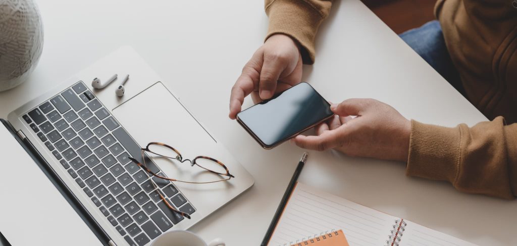 開業資金の調達方法や手続きについてスマートフォンとパソコンを使ってリサーチしている男性の手元