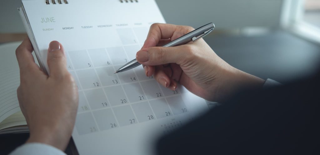 売上債権の入金期日が近づいていることを確認するために卓上カレンダーの日付をペンで指している手元