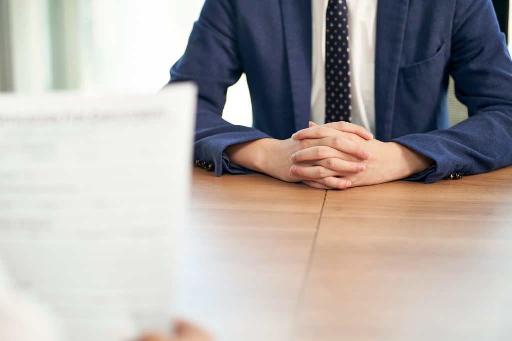 机の上で手を組み対面に座るスーツ姿の男性。プロパー融資を受けるために銀行担当者と面談を行ったり審査を受けている場面