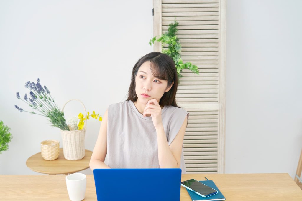 ノートパソコンの前で頬に手を当てて資金繰りやファクタリングの利用について真剣に悩んでいる女性の様子