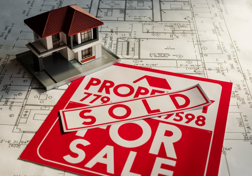 中小企業の資金調達における不動産担保融資や資産売却をイメージさせる、建築図面上の住宅模型とSOLDの看板