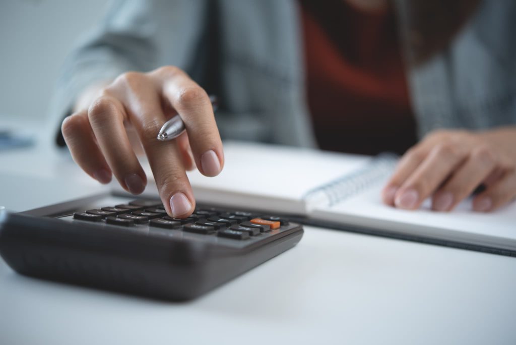 電卓を操作して計算する手元。ファクタリングを利用する際にかかる手数料や実質金利を相場と照らし合わせながら算出している様子