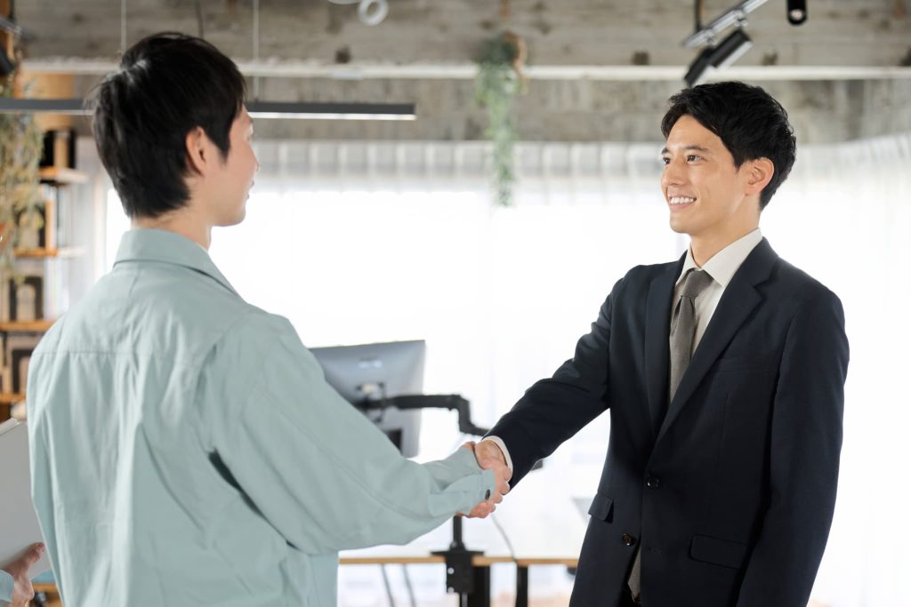 中小企業の資金調達交渉が無事に成立し、経営者と金融機関の担当者が笑顔で握手を交わしているビジネスシーン