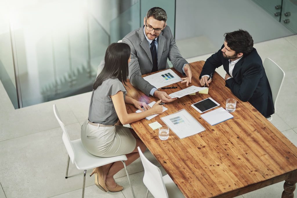 請求書の立替払いサービスの導入について資料を見ながら打ち合わせを行う3人のビジネスパーソンの様子