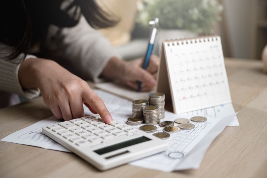 ファクタリングの乗り換え前後の費用対効果を比較するために硬貨と電卓を使って収支計算をしている手元