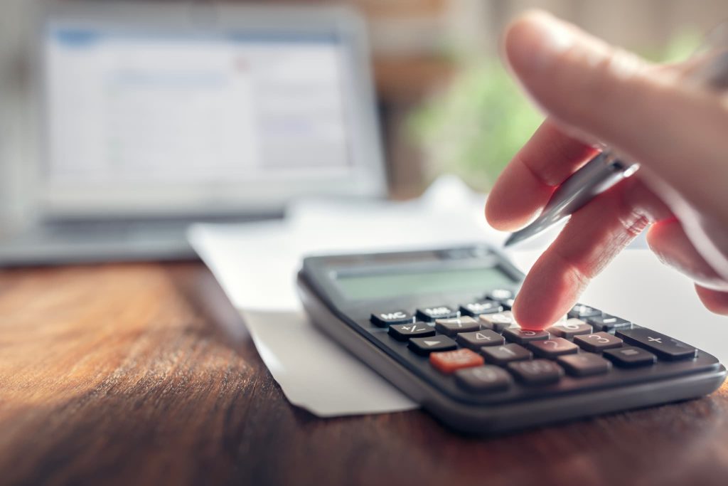 ノートパソコンの前で電卓を使い計算する様子。助成金や補助金など、返済不要な資金調達を計画する際に、対象経費や受給予定額を慎重に算出している手元