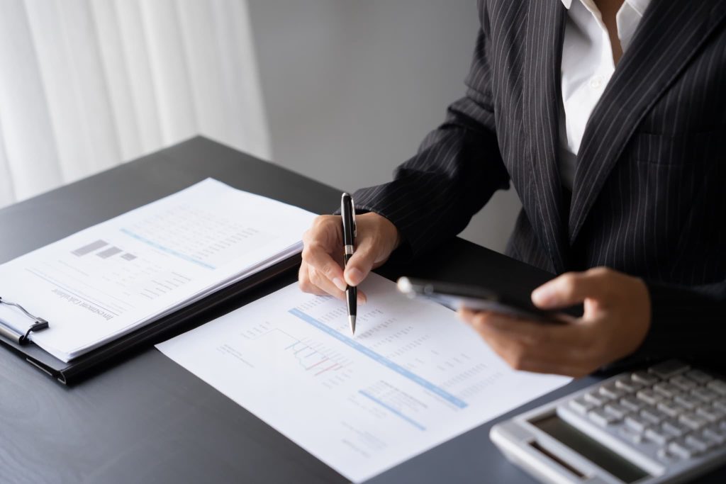 資料とスマートフォンを持ちグラフを確認するスーツ姿の人物。短期借入金と長期借入金の比率を見直し財務状況を分析している経営企画の場面