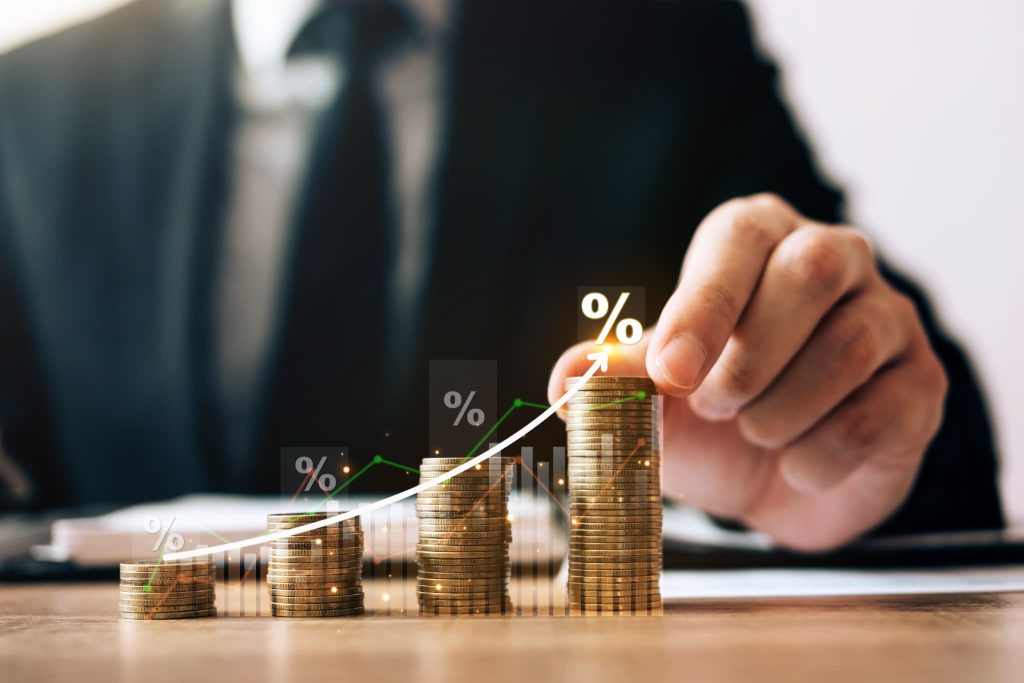 高さが異なる積み上げられたコインと、上昇する矢印やパーセント記号。金利コストを考慮した返済計画や、事業成長に伴って必要となる増加運転資金の調達をイメージさせる