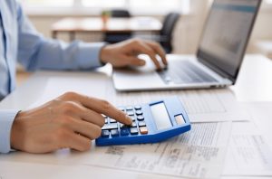 売掛金のファクタリングと受取手形の手形割引の違いを比較検討し、2027年の手形廃止に備えて新たな資金調達手段をパソコンと電卓で模索する様子