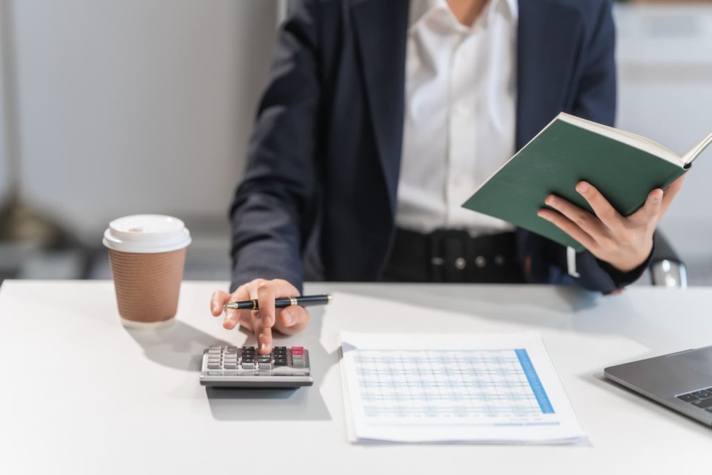 2社間ファクタリングや3社間ファクタリングの利用に向け帳簿を確認しながら電卓を叩く経理担当者の手元