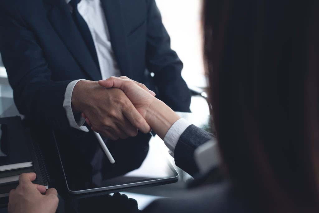ファクタリングの利用や返済条件について合意し信頼の証として握手を交わすビジネスマンと担当者