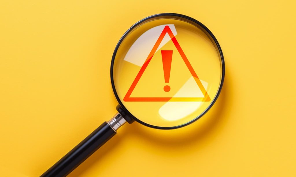 虫眼鏡で拡大表示された赤い警告マーク。飲食店が資金調達を行う際の注意点やリスク、融資審査における重要なチェックポイントを強調している