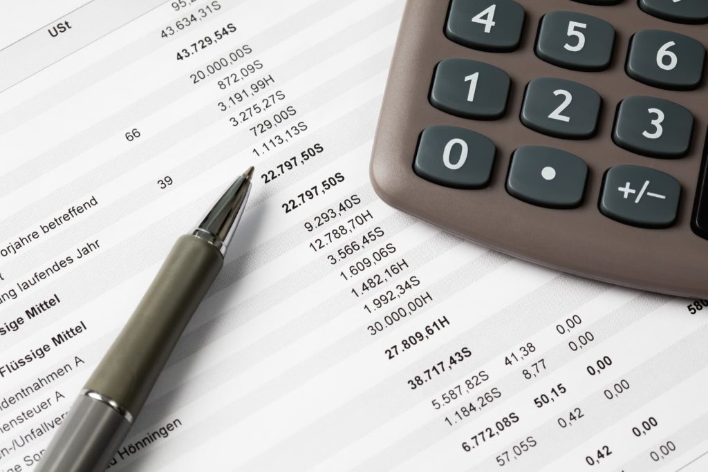 数字が羅列された財務書類の上に置かれたボールペンと電卓。キャッシュフローを正確に計算・管理し、企業の資金繰りや財務状態を細かくチェックしている経理業務の様子