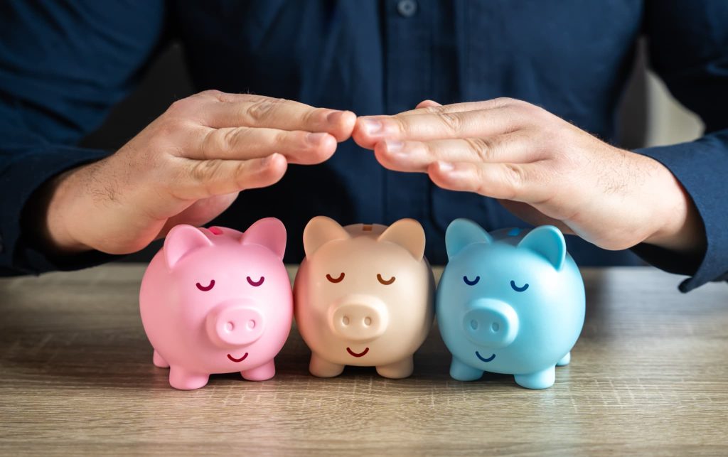 経営努力による固定費削減で守られた利益や資産を象徴する3つの貯金箱とそれを保護するように覆う手