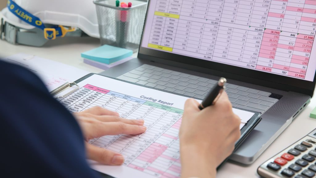 事務所でCosting Reportと書かれた原価管理表にペンで書き込みファクタリングのメリットデメリットをコスト面から確認している手元