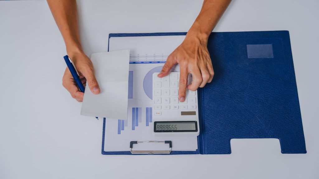 グラフ資料の上で電卓を叩く手元。日々の経費精算や収支計算を行い、事業運営に必要な運転資金の残高を正確に把握しようとしている経理業務のワンシーン