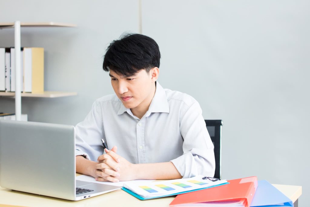 ノートパソコンの画面を真剣な表情で見つめ手を組む男性。ビジネスローンのデメリットや審査通過の可能性について慎重に情報を集めている様子
