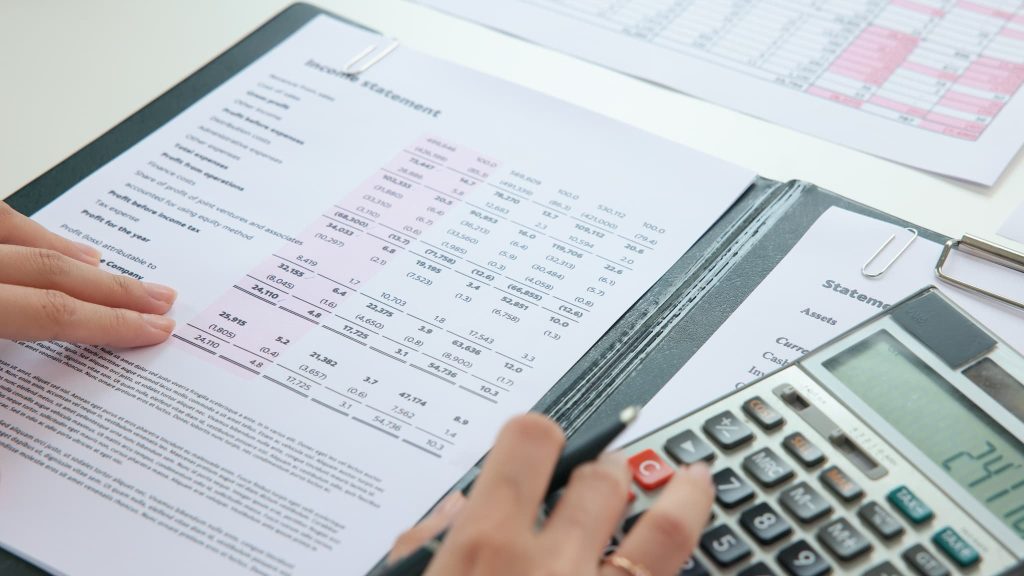 請求書カード払いサービスの手数料を経費として計上するために財務諸表や帳簿を確認しながら電卓で計算している様子