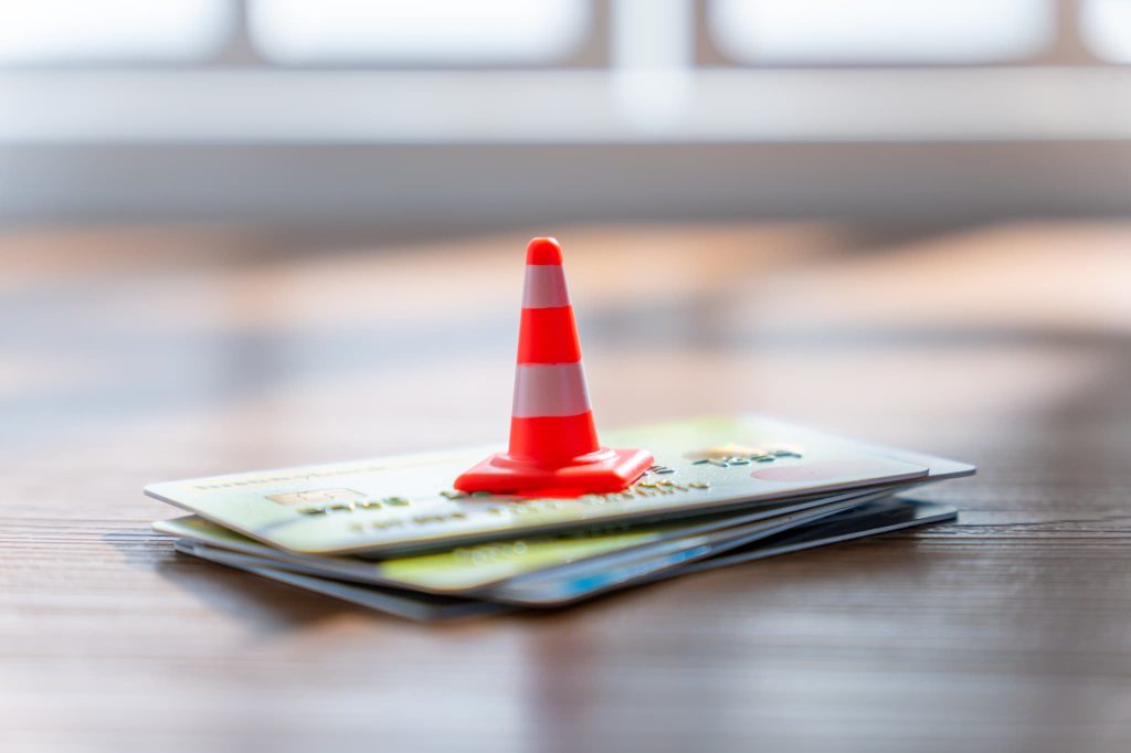 個人事業主がカードローンを利用する際の使いすぎや返済遅延などのリスクを警告するカラーコーンとカードの山