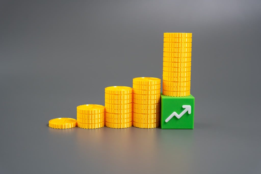 右肩上がりに積まれた黄色いコインと上昇矢印のブロック。健全なキャッシュフロー経営によって資金が順調に増加し、企業が成長していく過程を表現したイメージ
