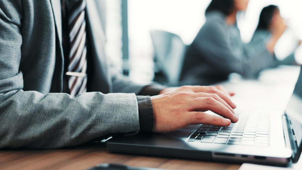 オフィスでノートパソコンのキーボードを操作して入力作業を行っている男性の手元のアップ。ノンバンクへのWeb申し込みや審査手続き、事務処理を行っているビジネスの様子