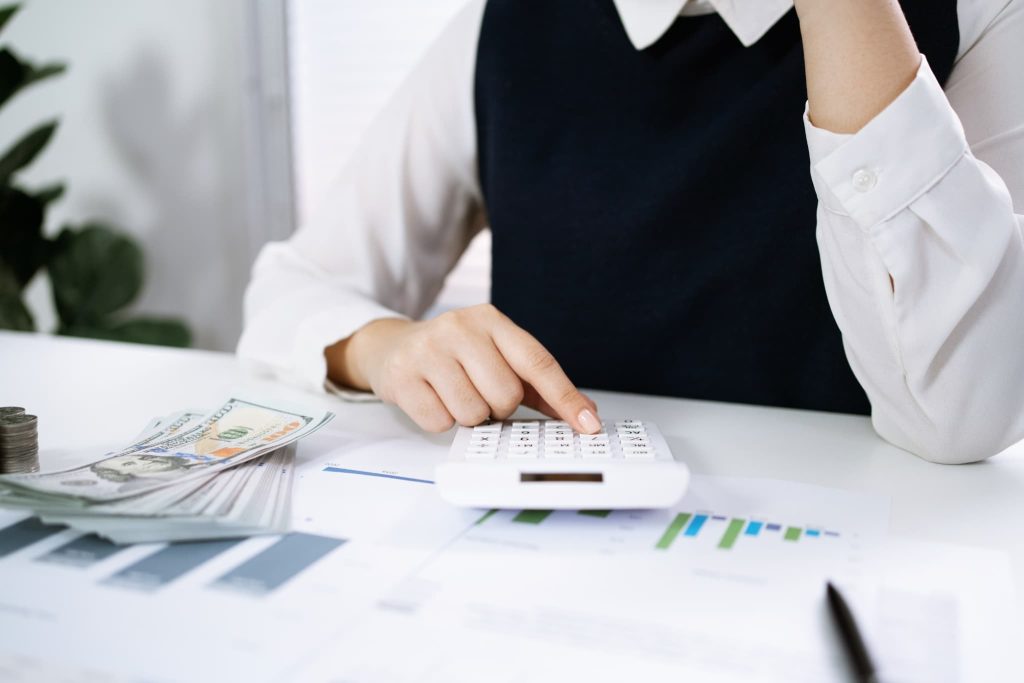 電卓を叩く手元と積まれた紙幣。債務超過とは資産よりも負債が多い状態を指し、現状の財務状況を計算し確認している経理業務の様子