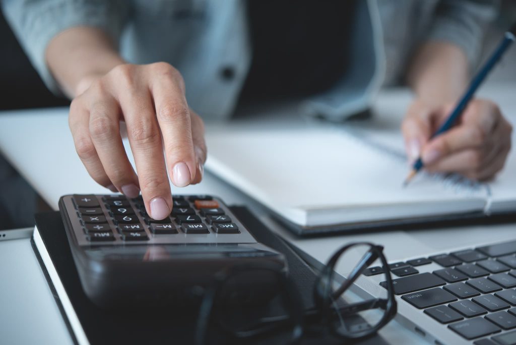 補助金と助成金の対象経費の違いを確認しながら電卓とパソコンを使って試算を行っている女性