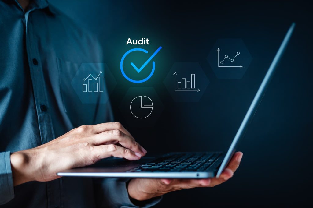 パソコン画面上に浮かぶ「Audit」の文字とチェックマーク、グラフのグラフィック。キャッシュフロー改善に必要な財務監査やデータ分析をデジタル技術で行うイメージ