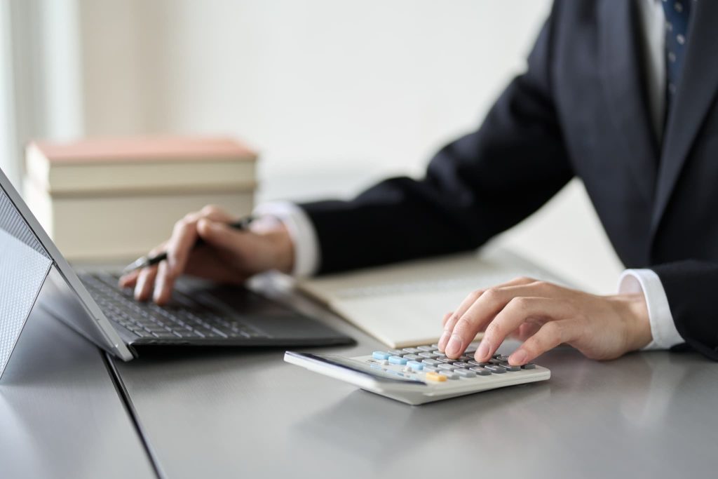 督促状の作成や未回収金の計算業務を行うためにパソコンと電卓を操作している経理担当者の手元