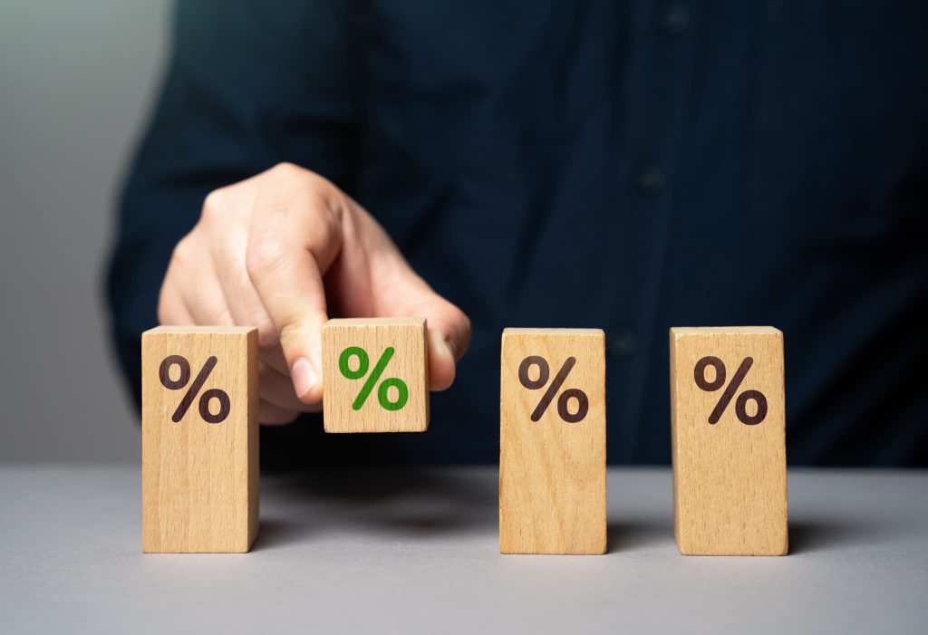 パーセント記号が記された木製ブロックを選ぶ手元。ファクタリングの手数料率や金利の相場がどの程度か比較検討しているイメージ