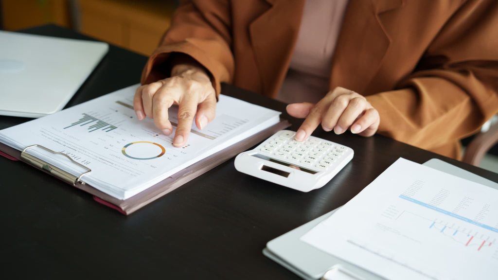 予算報告書の円グラフを確認しながら電卓を叩きファクタリングのメリットデメリットを数値に基づいて詳細に分析している様子