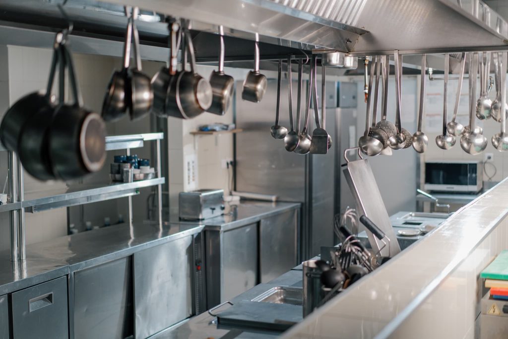 業務用厨房に整然と吊り下げられた調理器具とステンレス製の設備。飲食店経営で大きな比重を占める厨房機器導入や設備資金の調達に関連する様子