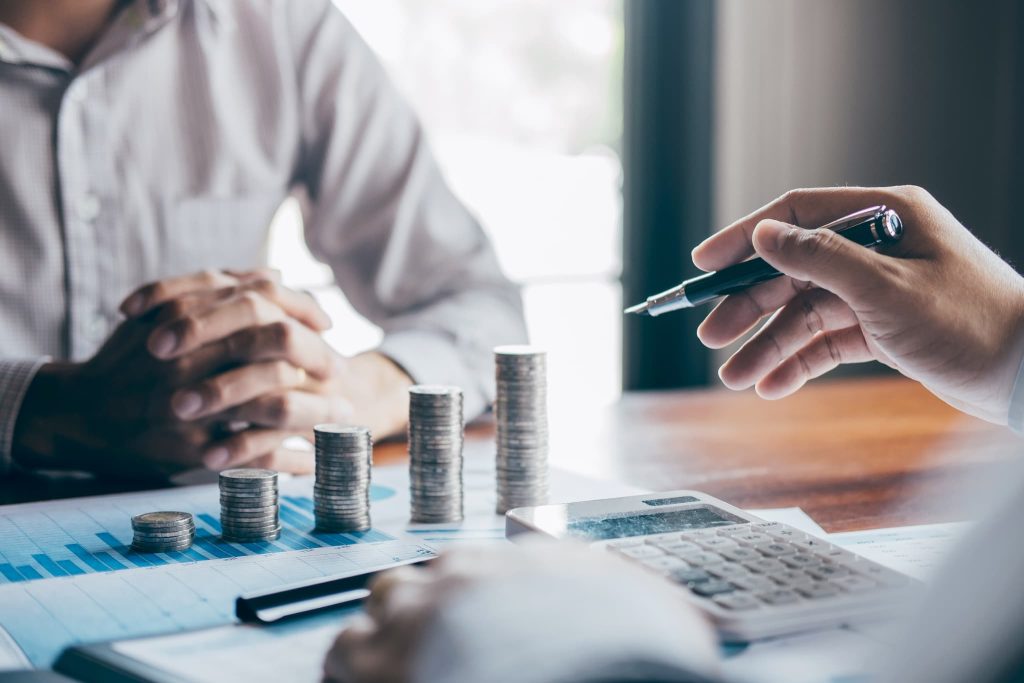 デスクに積み上げられたコインと、対話するビジネスマン。「資金調達とは」すなわち事業に必要な資金を外部から確保し、企業の成長のために投資することを視覚的に表現している