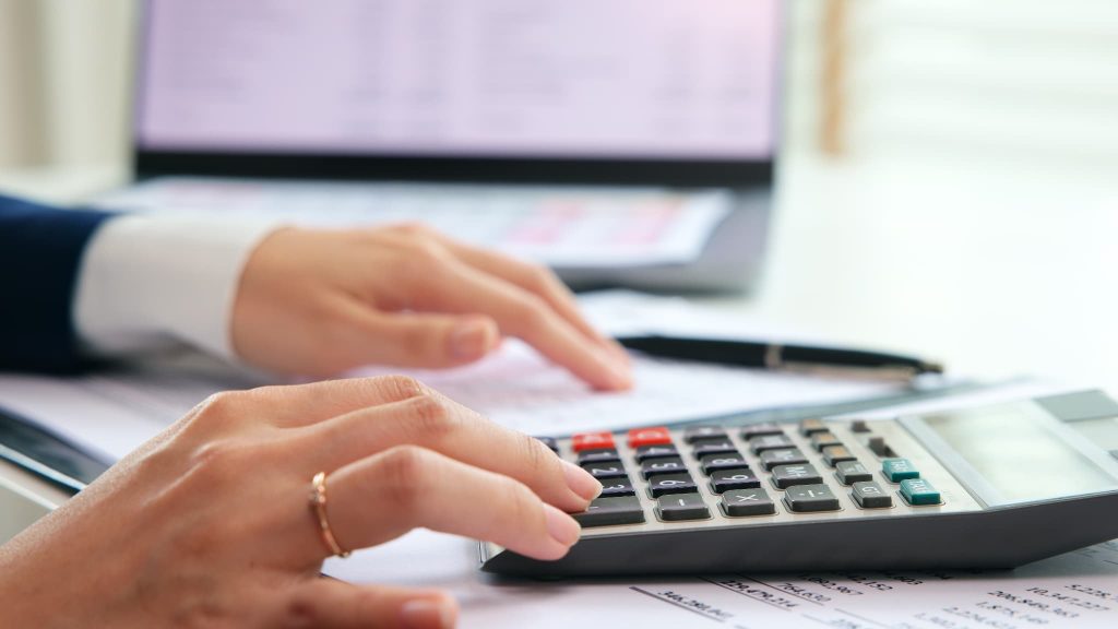 ファクタリングで調達した資金の返済スケジュールや手数料を電卓とパソコンを使って計算している女性