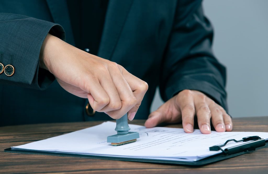 新しい業者へのファクタリングの乗り換えが決まり契約書に判子を押して手続きを完了させるビジネスマン