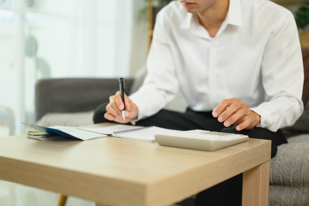 通帳と電卓を机に置き、中小企業の資金調達や返済計画について頭を抱えて悩んでいる若い経営者