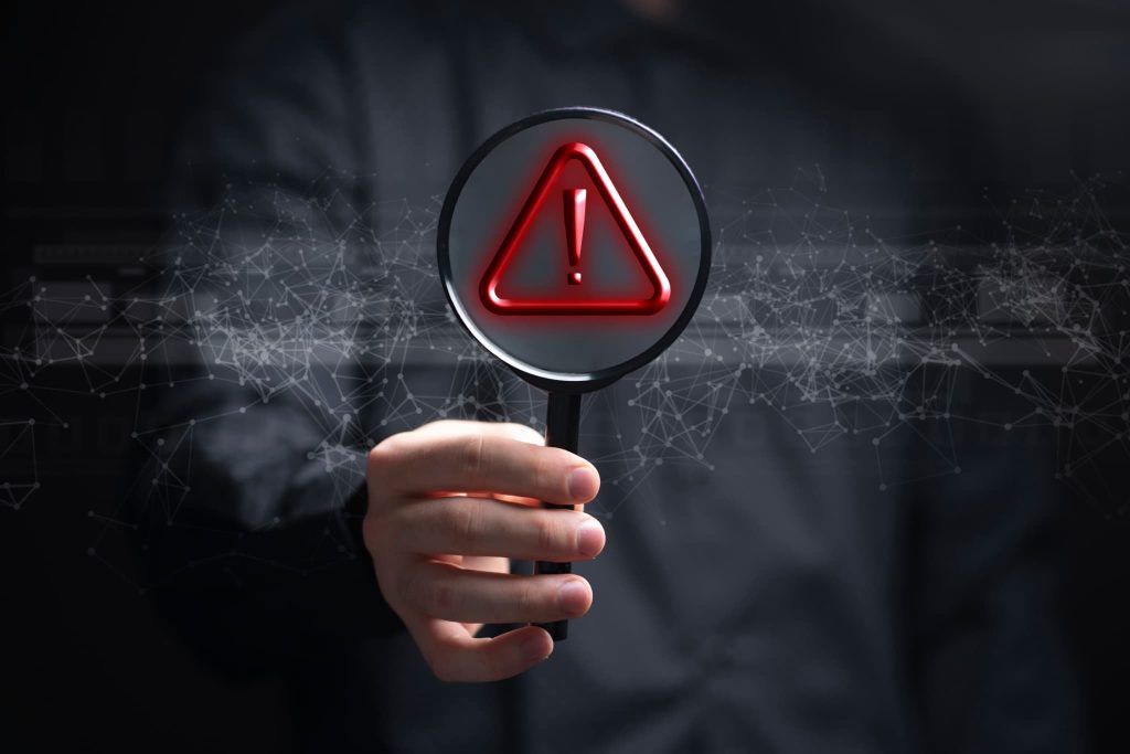 虫眼鏡で拡大された赤色の警告マーク。債務超過とは企業の安全性における危険信号であり、見過ごすと倒産につながる重大なリスクであることを示すイメージ